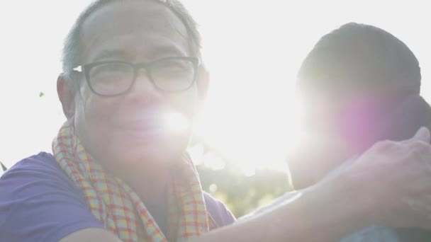 Onnellinen vanhempi isoisä silmälaseissa halaa nuorta lapsenlastaan pihalla aamun auringonvalossa. Syleily, joka ilmaisee rakkautta ja sidettä kahden sukupolven välillä perheessä. - Materiaali, video