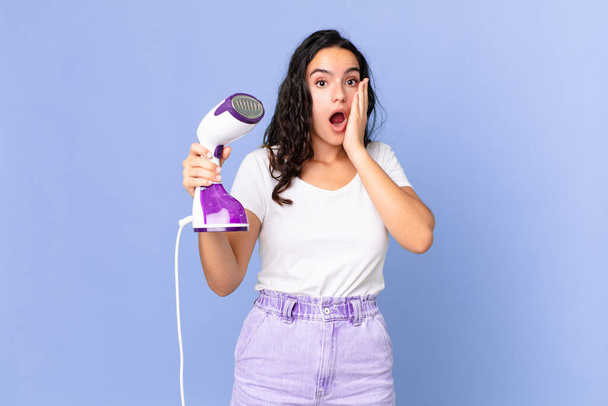 hispanic pretty woman feeling shocked and scared and holding an iron steam - Photo, Image