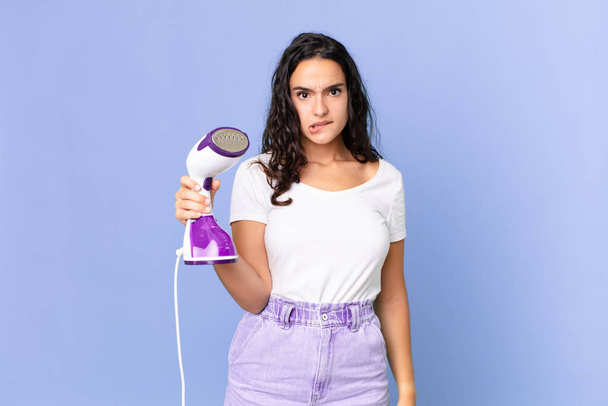 hispanic pretty woman looking puzzled and confused and holding an iron steam - Photo, Image