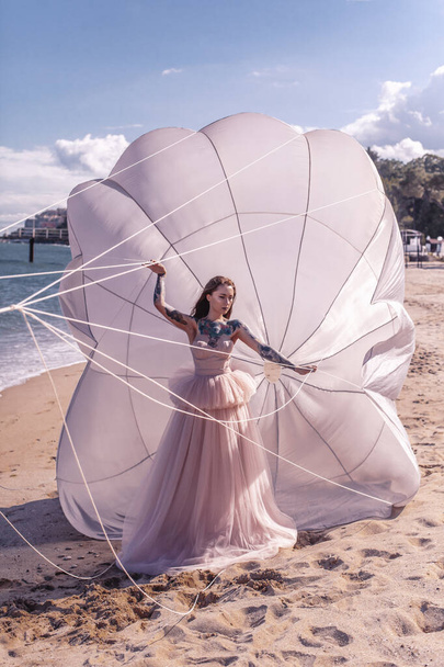 Mooie vrouw met witte parachute aan het strand - Foto, afbeelding