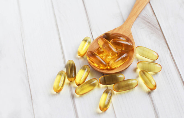Fish oil capsules on wooden background and texture, Fish oil capsule placed on a wooden spoon, spot focus. - Photo, Image