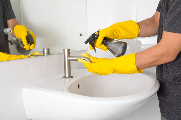 hands in yellow gloves cleaning sink in bathroom. Disinfecting bathroom. Prevention of coronavirus infection - Photo, Image