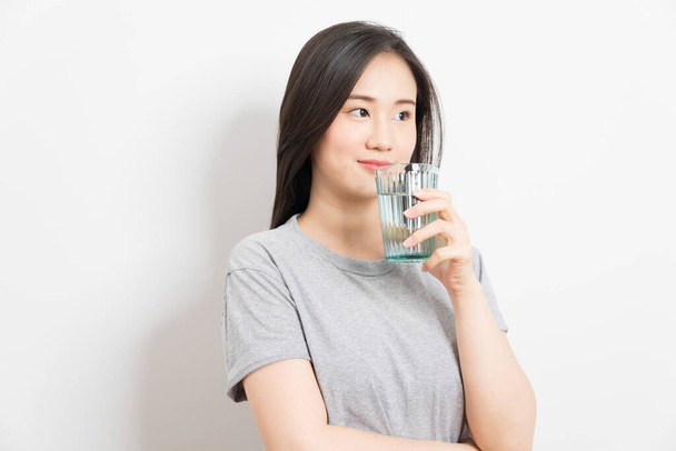 Schöne junge asiatische Frau trinkt Glas Mineralwasser, glücklich zu Hause. - Foto, Bild