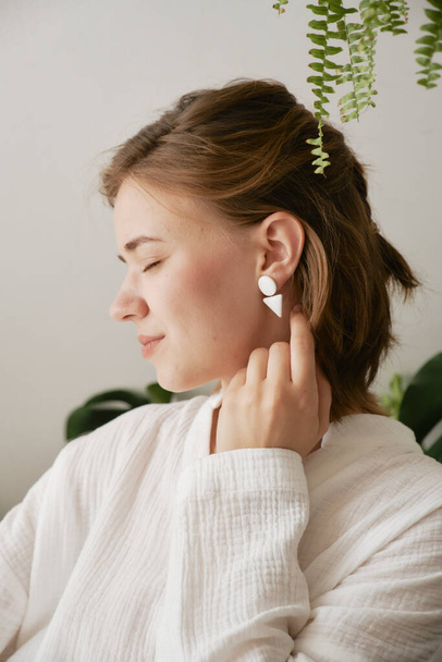 Cute girl in white ceramic earrings in the form of geometric shapes. Handmade jewelry. - Фото, изображение
