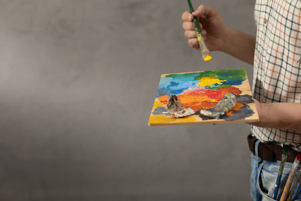 Man painter holding paint palette with paint brush. Young artist and paintbrush painting in creative studio - Fotó, kép