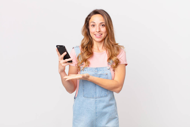 pretty woman smiling cheerfully, feeling happy and showing a concept and holding a smartphone - Foto, immagini
