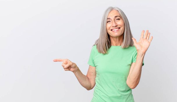 middle age white hair woman smiling happily, waving hand, welcoming and greeting you and pointing to the side - Φωτογραφία, εικόνα