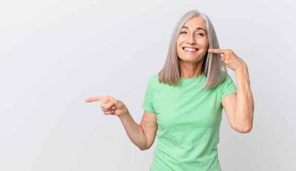 middle age white hair woman smiling confidently pointing to own broad smile and pointing to the side - 写真・画像