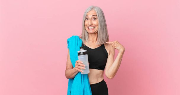 middle age white hair woman feeling happy and pointing to self with an excited with a towel and water bottle. fitness concept - Фото, изображение