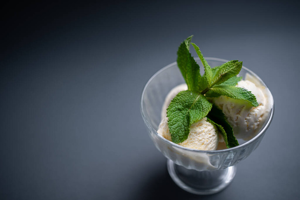 tasty vanilla ice cream with fresh mint in glass bowl on black background - 写真・画像