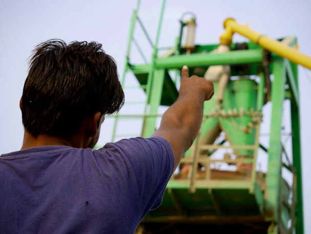 Un trabajador masculino indio apuntando con el dedo hacia una máquina mezcladora de concreto alrededor del fondo industrial del cielo. - Foto, imagen