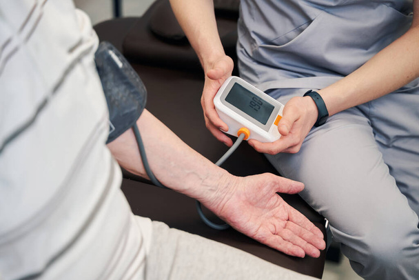 Medical worker using blood pressure monitor on pensioner - Photo, Image