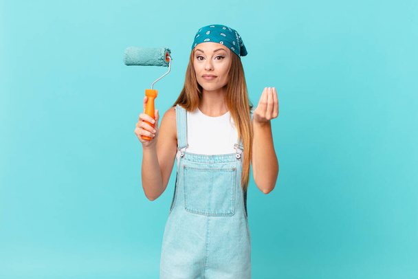 pretty woman making capice or money gesture, telling you to pay painting a new home wall - Fotoğraf, Görsel