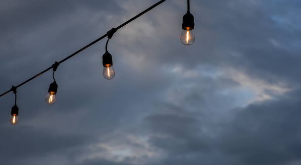 曇った夜の空を背景に電球 - 写真・画像