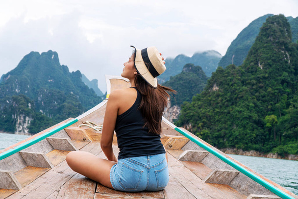 Adventure lifestyle vacationer relax concept. Traveler young woman wear hat sitting on long tail boat floating lagoon with mountains and sky while vacation tourist  at surat thani. - Photo, Image
