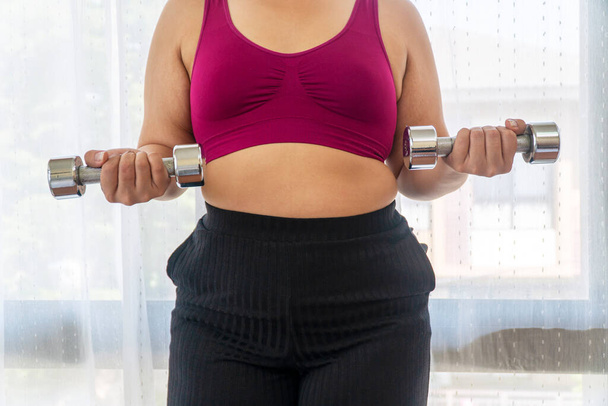 Aktivität Bewegung fit Körper für Ernährung oder Fettleibigkeit Konzept. Positiv glückliche übergewichtige, dicke Frau, die Hanteln in den eigenen Händen hält, trainiert Gewichtsabnahme, während sie im Raum steht. - Foto, Bild
