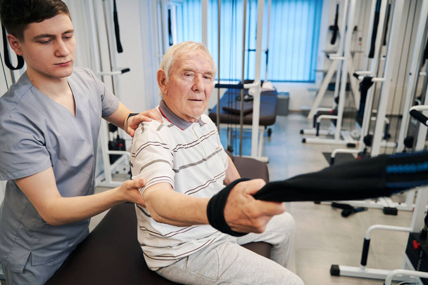 Confident senior citizen doing arm exercise on rehabilitation equipment - Photo, Image