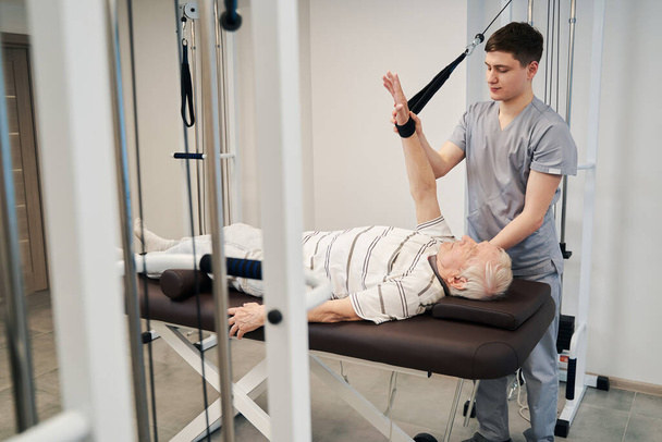 Medical specialist moving man arm during rehabilitation training - Photo, Image
