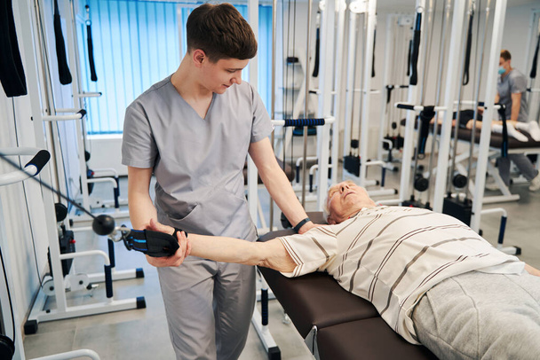 Физиотерапевт опускает руку пенсионера в сторону во время упражнений по отстранению - Фото, изображение