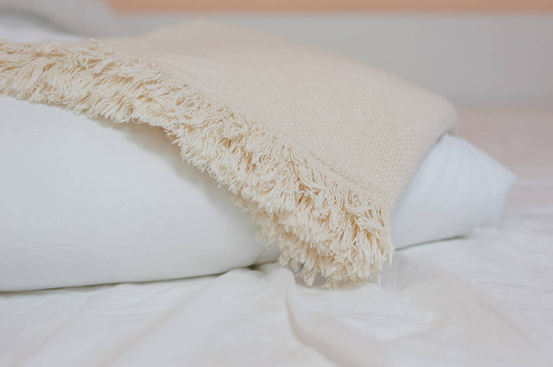 Egy halom fehér párna és takaró fekszik az ágyon egy fehér lepedőn a tetején, takaróval borítva. - Fotó, kép