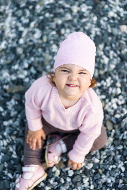 portret mały piękny uśmiech dziewczynka w różowej kurtce siedzi na kamieniach, beztroskie szczęśliwe dzieciństwo - Zdjęcie, obraz