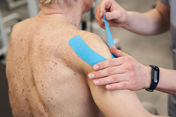Médico aplicando cinta de kinesiología al hombro del hombre anciano - Foto, Imagen