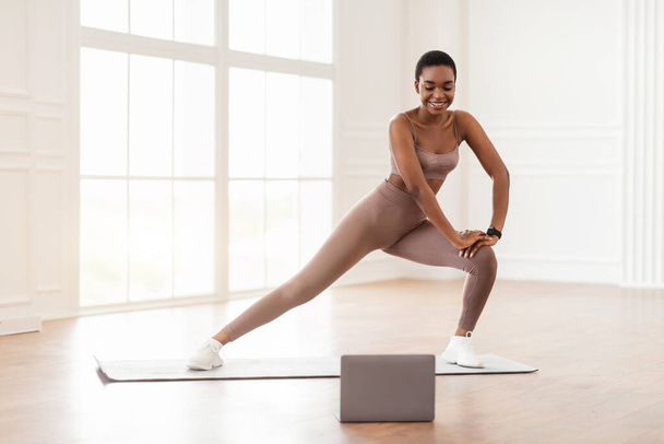 Young black woman doing side lunges on mat using pc - Photo, Image