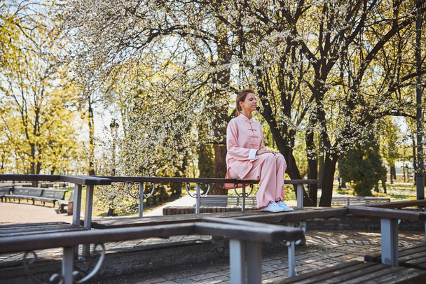 Meditating woman in pink sitting on bench in sunny park - Foto, Imagen
