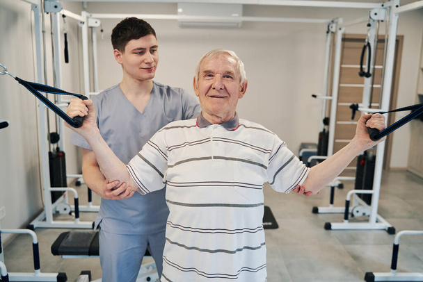 Senior patiënt trekken touwen van fitnessapparatuur van beide zijden - Foto, afbeelding
