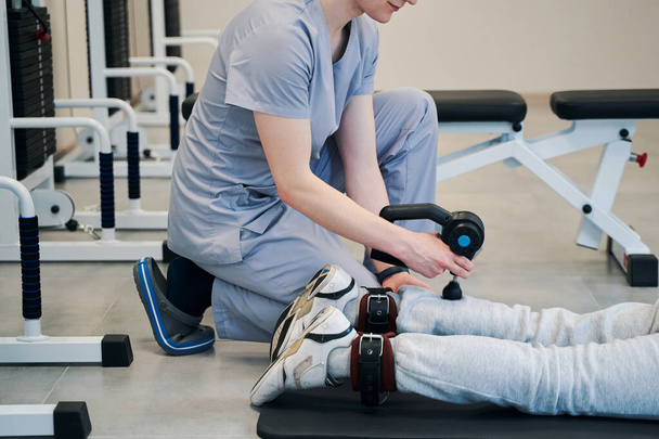 Medic met diepe weefsel massage pistool werken op patiënt been - Foto, afbeelding