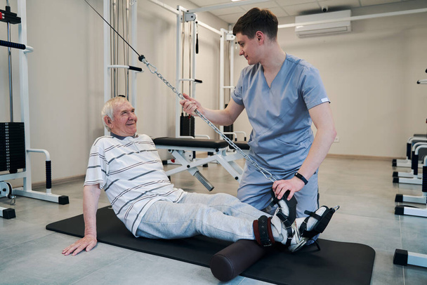 Старый пациент улыбается доктору во время работы системы веса шкива - Фото, изображение