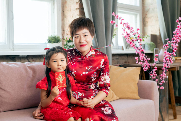 Matka a dcera v červených šatech sedí na gauči - Fotografie, Obrázek