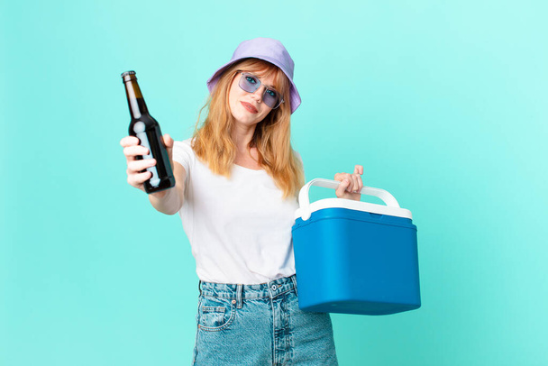 pretty red head woman with a portable refrigerator and a beer - Foto, Imagen