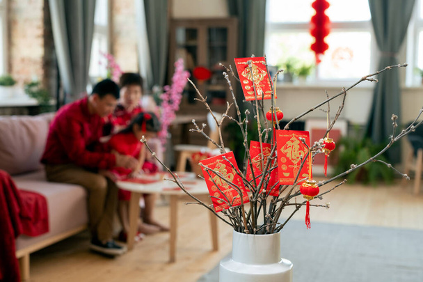 Red new year postcards and lanterns hanging on dry branches in white vase - Photo, Image