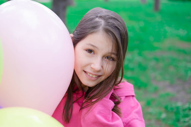 hezká mezi teenager brunetka dívka v růžové drží barevné horkovzdušné balónky venku. párty, narozeninová koncepce. v létě. Šťastné děti. dovolená, letní prázdniny. - Fotografie, Obrázek