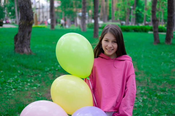 hübsches brünettes Teenager-Mädchen in rosa mit bunten Heißluftballons im Freien. Party, Geburtstagskonzept. Sommerzeit. Glückliche Kinder. Feiertage, Sommerpause. - Foto, Bild