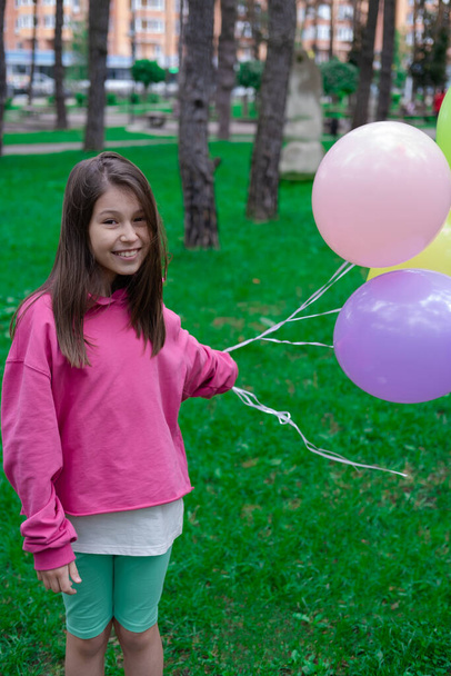 hübsches brünettes Teenager-Mädchen in rosa mit bunten Heißluftballons im Freien. Party, Geburtstagskonzept. Sommerzeit. Glückliche Kinder. Feiertage, Sommerpause. - Foto, Bild