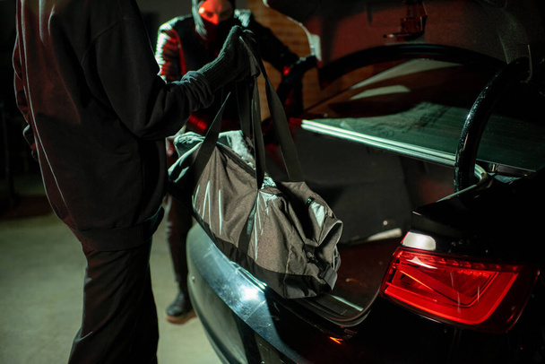 Two hackers putting bag into car-back - Photo, Image