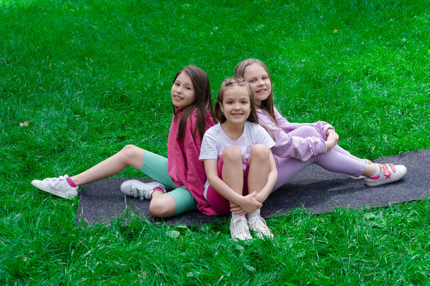 公園の緑の草の上に座ってカラフルな服を着た10代の女の子の間で3つの美しい幸せ。夏だ。幸せな子供たち。休日や夏休み。姉妹、親友、 BFF 、姉妹. - 写真・画像