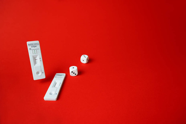 Rapid SARS-Cov-2 Antigen Test,negative result and unused,2 dice on red background.Concept of bad luck,be healthy or get infected during pandemic.Playing game with fate.Unreliable results probability. - Foto, imagen