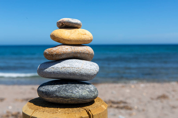 Ausgeglichenheit und Schönheit in pyramidenförmiger Form aus fünf Steinen, die übereinander im Gleichgewicht stehen und dem Meer zugewandt sind, was Frieden und visuelle Harmonie verleiht. - Foto, Bild