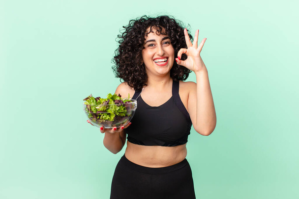 pretty arab woman feeling happy, showing approval with okay gesture and holding a salad. diet concept - Zdjęcie, obraz