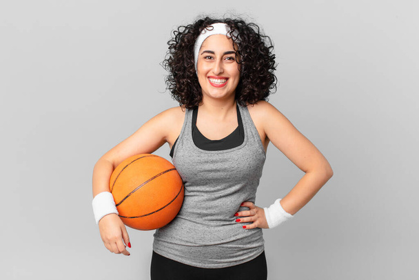 pretty arab woman smiling happily with a hand on hip and confident and holding a basketball ball. sport concept - Foto, Imagem