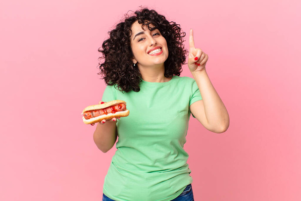 pretty arab woman feeling like a happy and excited genius after realizing an idea and holding a hot dog - Foto, Imagem