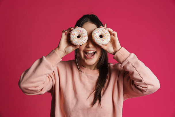 Happy young woman posing holding donuts over pink wall background - Фото, изображение