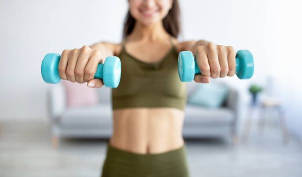 Cropped view of young Indian lady exercising with dumbbells at home during coronavirus epidemic, selective focus - Foto, imagen