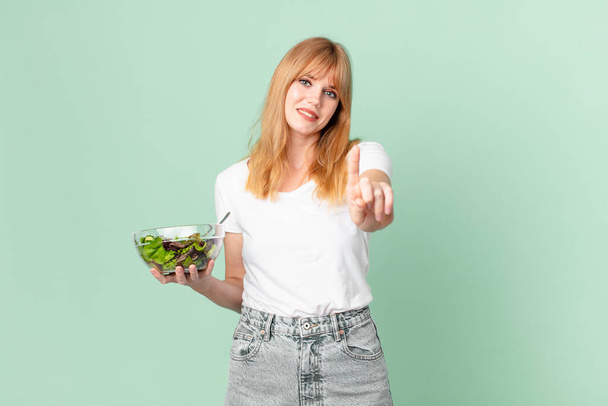 pretty red head woman smiling proudly and confidently making number one and holding a salad. diet concept - Photo, image