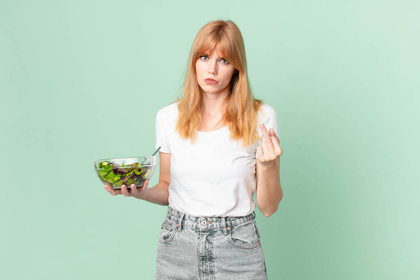 pretty red head woman feeling angry, annoyed, rebellious and aggressive and holding a salad. diet concept - Fotó, kép