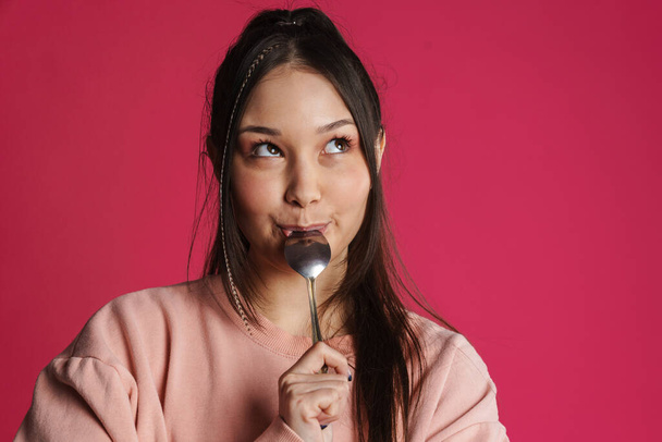 Asian brunette happy woman licking her spoon and looking at camera isolated over purple wall - Valokuva, kuva