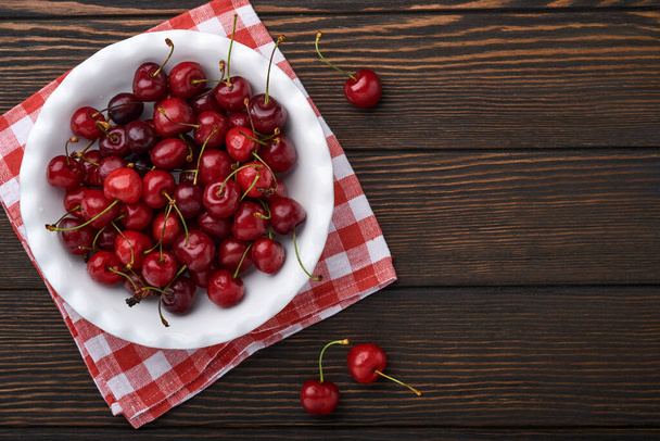 Cherry with water drops on white bowl on dark brown stone table. Fresh ripe cherries. Sweet red cherries. Top view. Rustic style. Fruit Background - Fotografie, Obrázek